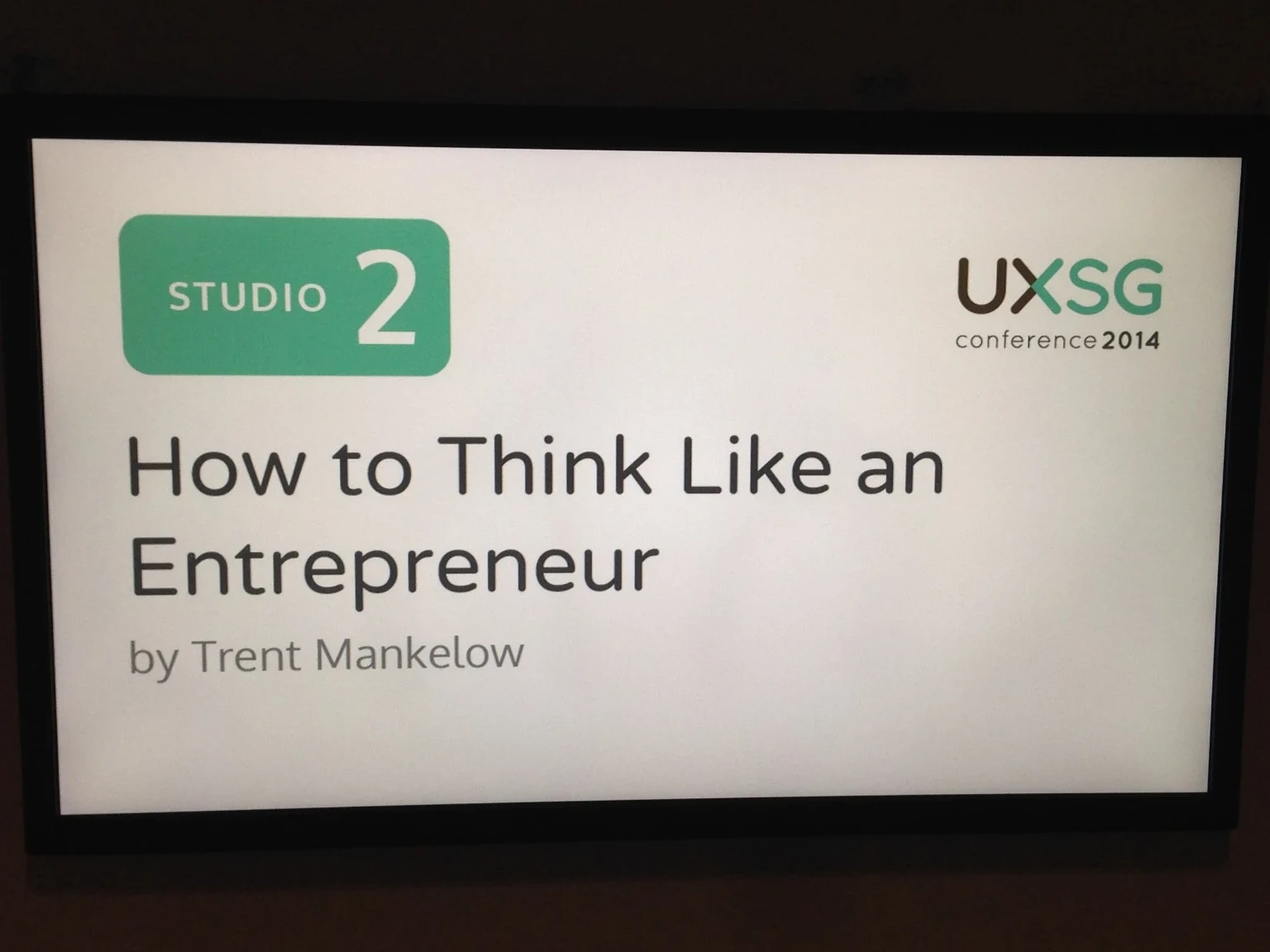 A screen reading 'How to Think Like an Entrepreneur by Trent Mankelow' at UXSG conference 2014